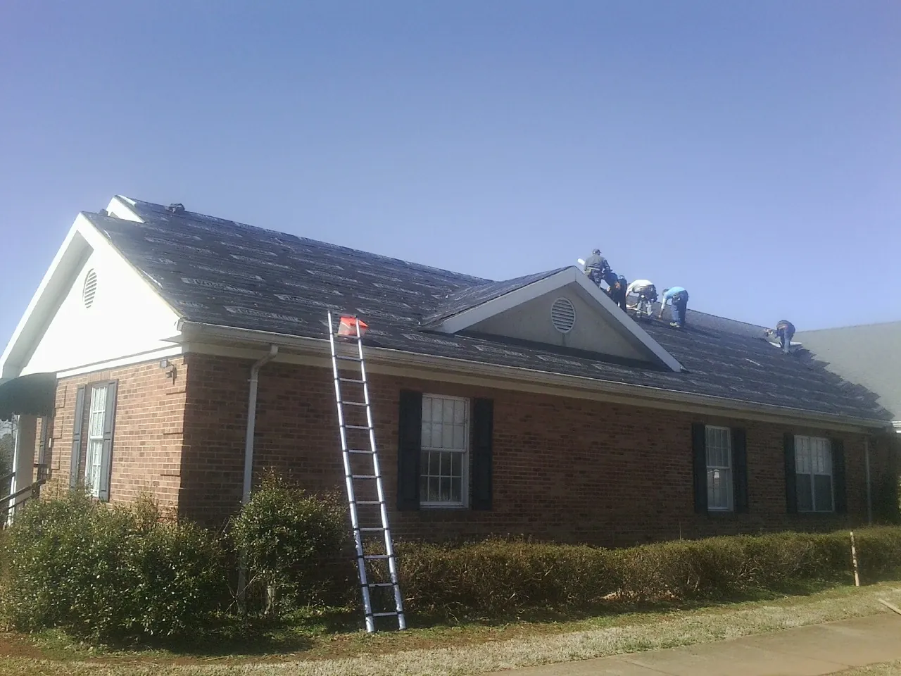 Crew tearing shingles off a brick ranch roof with a ladder set — Emergency Roof Repair work by our crew in Dorothy