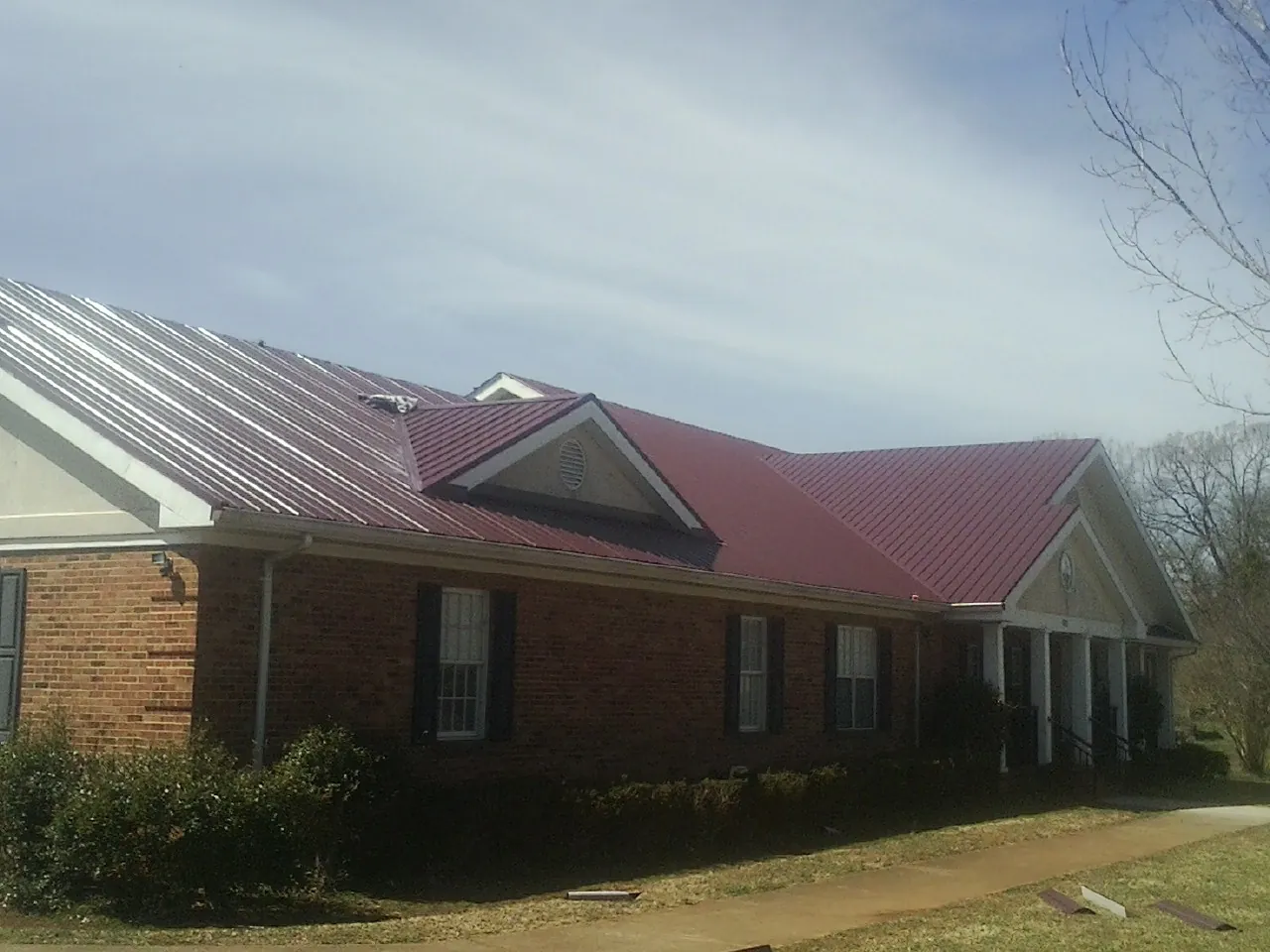 Red metal roof with gabled entries on a long brick building, from a Hail Damage Roof Repair job in Dorothy